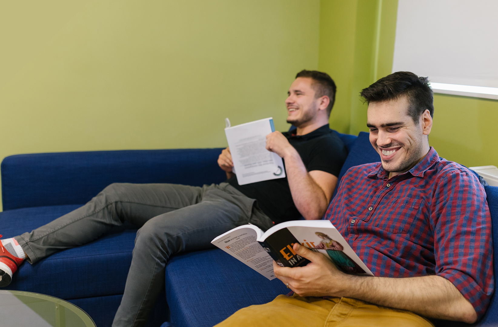 Two men sitting on a couch reading books.