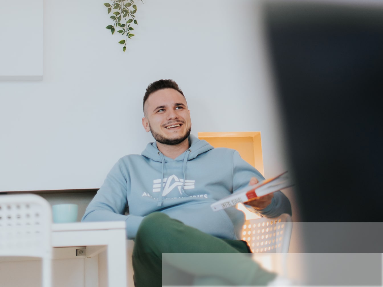 A smiling man sitting in an office lounge and holding a book
