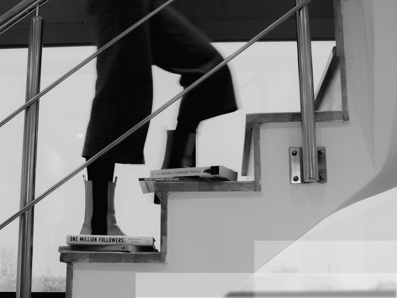 A woman climbing stairs with 4 books on steps, her legs visible in motion.
