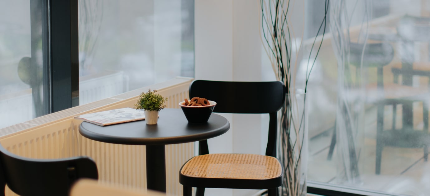 A table with cookies, magazine, and a small plant in an office lounge with two chairs nearby.